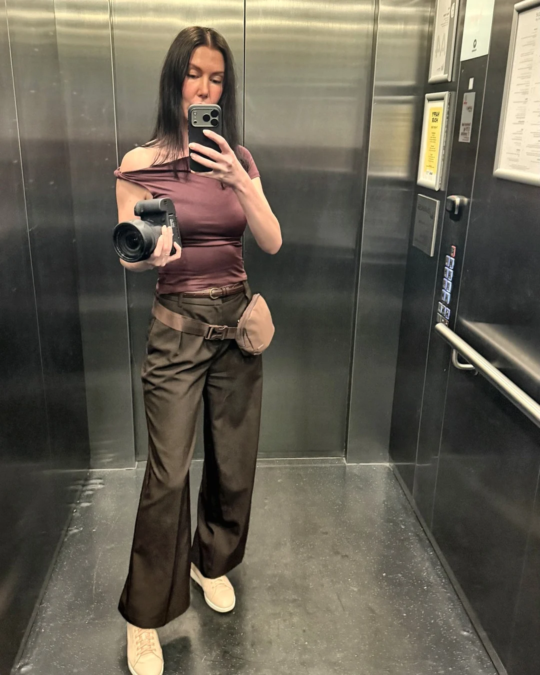 Melanie Laas taking a mirror photo on her phone in a lift, holding a camera
