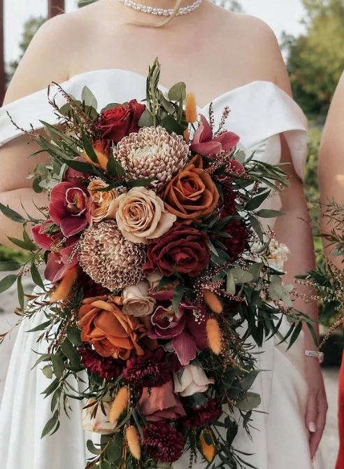 Detail of a cascading burgundy, rust and blush bridal bouquet against an off-shoulder gown